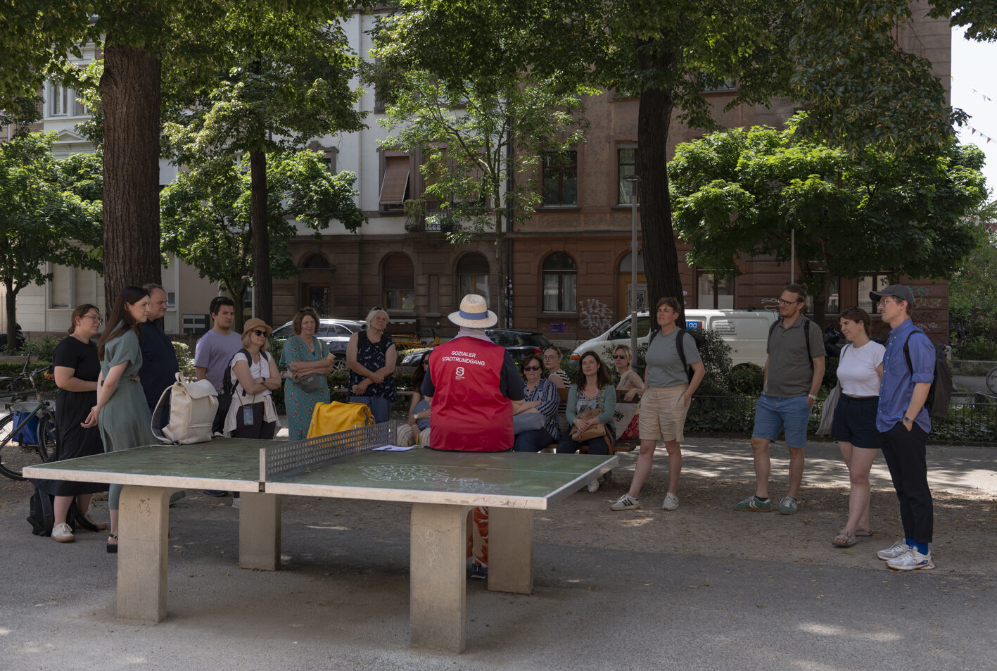 Eine Gruppe von Menschen steht um einen Tischtennistisch in einem Park.