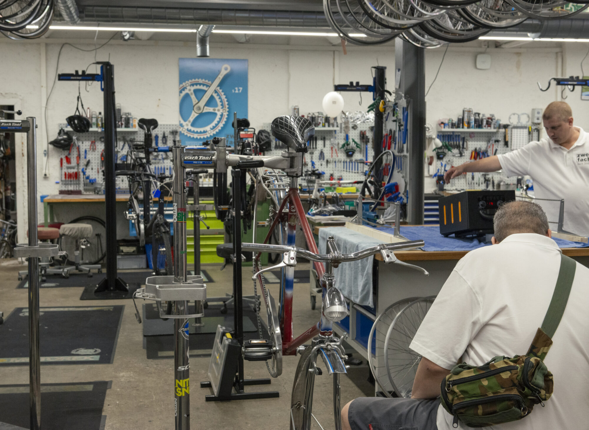zweifach Zwei Männer arbeiten in einer gut ausgestatteten Fahrradwerkstatt an verschiedenen Velos.