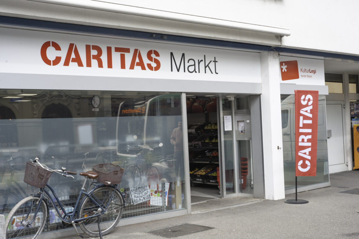Ein Fahrrad steht vor einem Caritas-Markt mit Obst- und Gemüseauslage.