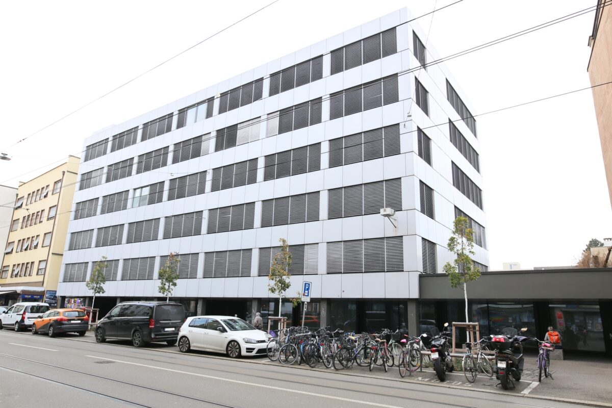 Ein modernes Gebäude mit Fahrrädern und Autos davor an einer Straße.