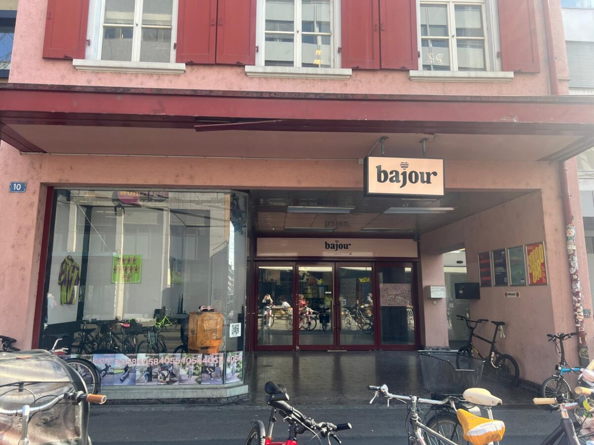 Ein Bild von einem Eingang mit Schaufenster. Über dem Eingang ist ein Schild mit dem Wort «Bajour». Im Vordergrund sind ein paar Velos zu sehen.