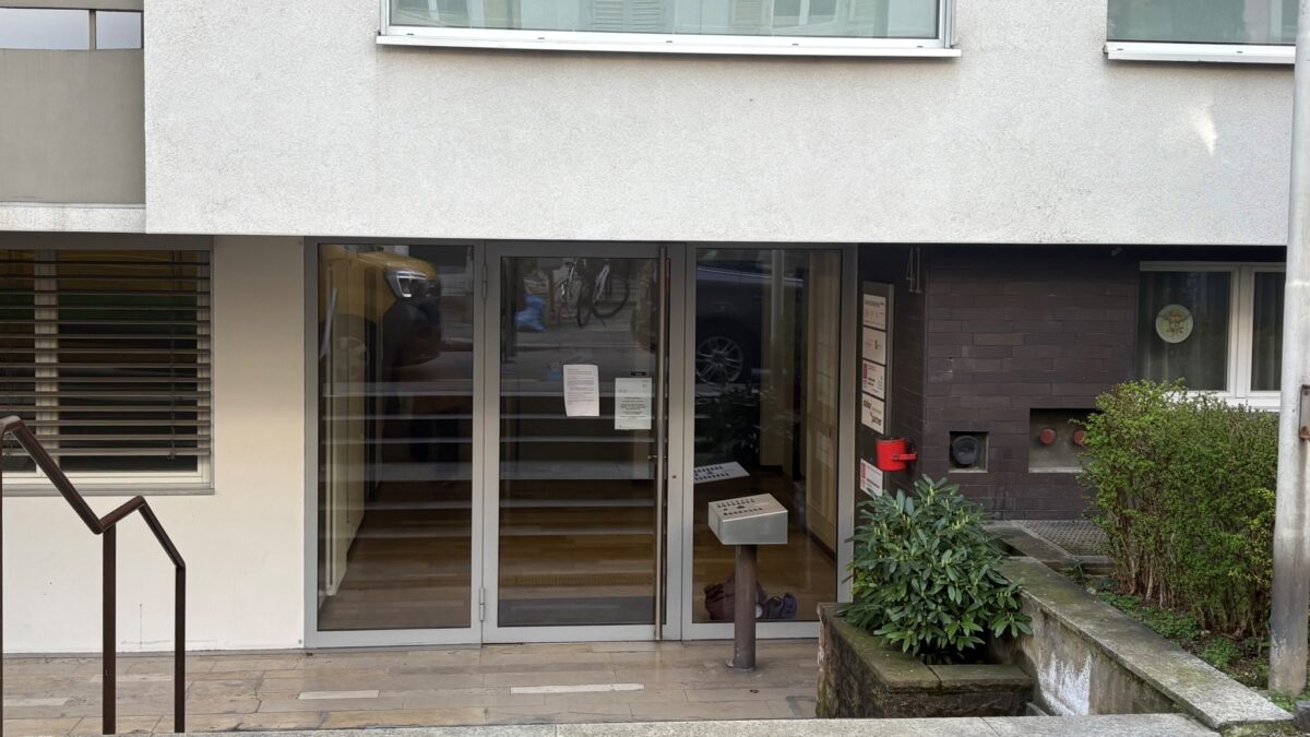 Glastüren eines Gebäudes mit Pflanze und Treppe daneben.