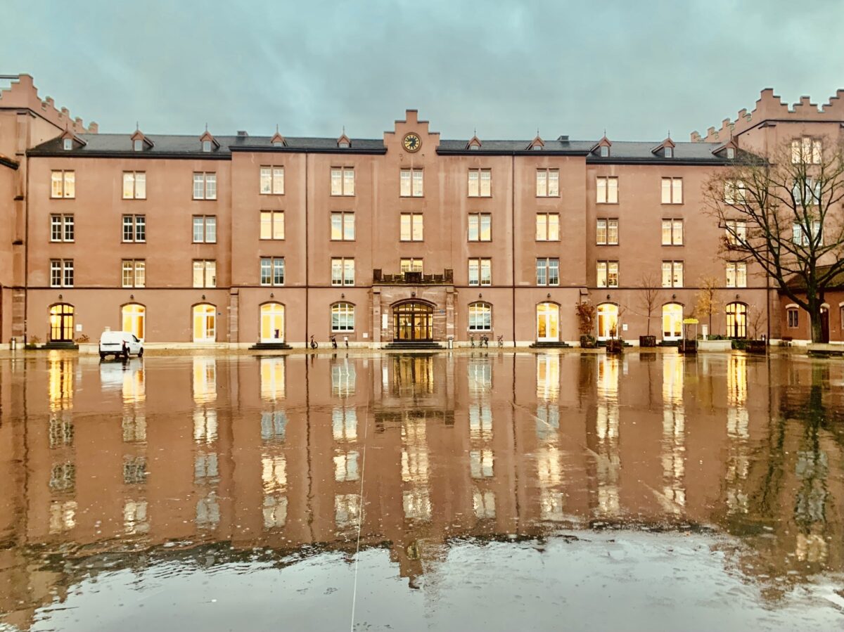 Ein großes Gebäude mit vielen Fenstern spiegelt sich in einer Pfütze wider.