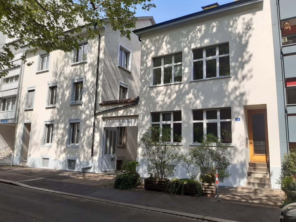 Ein weißes Gebäude mit mehreren Fenstern und einer Tür, an der "Steppenblüte" steht.