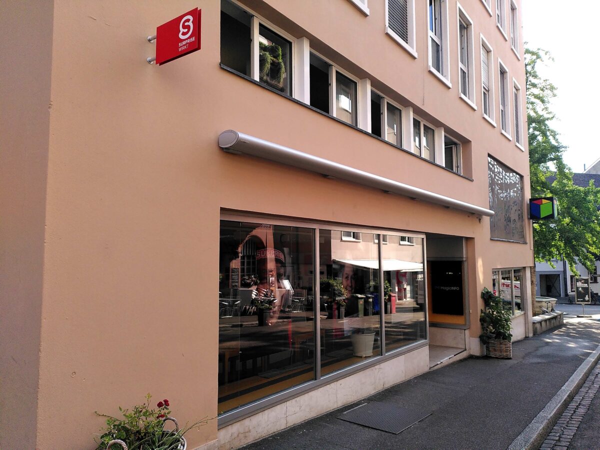 "Ein Café mit großer Glasfront an einer beigen Gebäudewand."