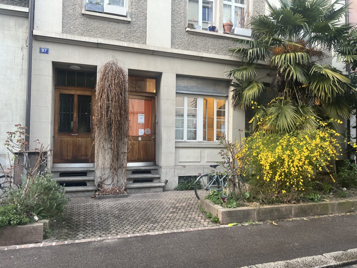 Ein Gebäude mit einer Holztür, Pflanzen und einem Fahrrad vor dem Eingang.