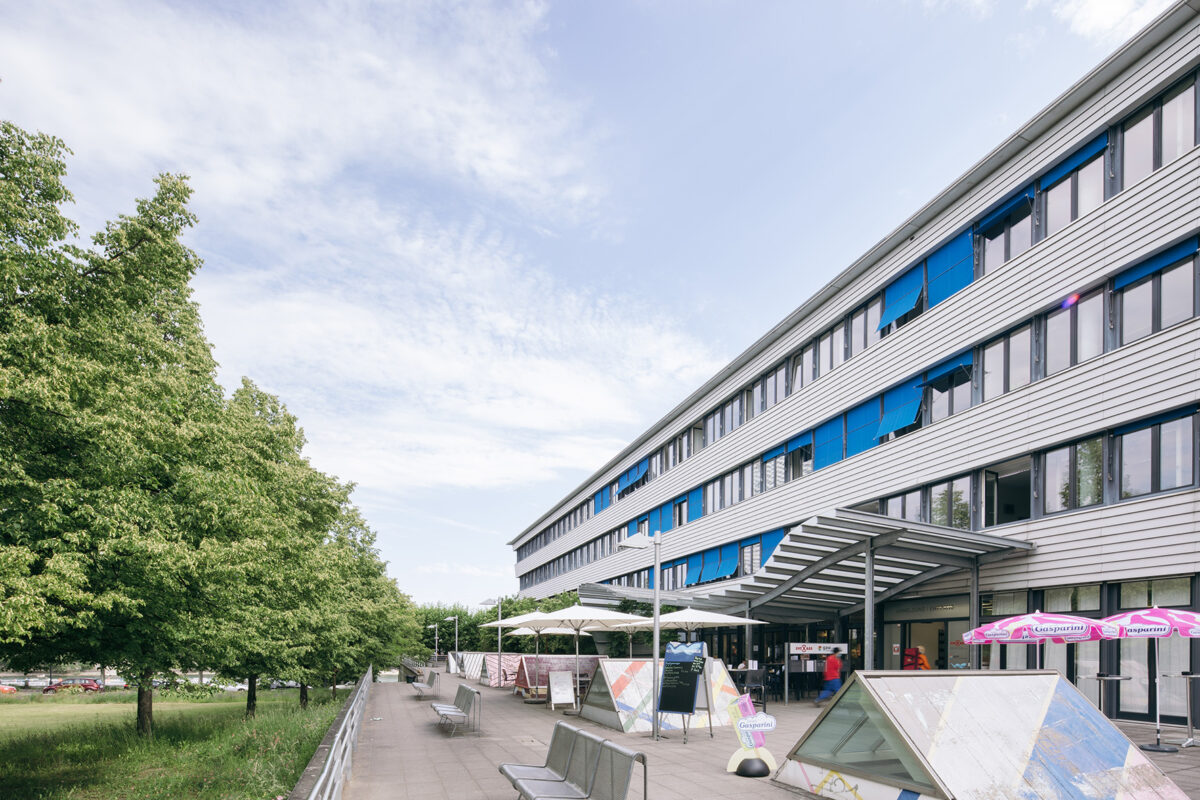 Moderne Gebäude mit blauen Markisen und Außensitzbereich mit Tischen und Stühlen.