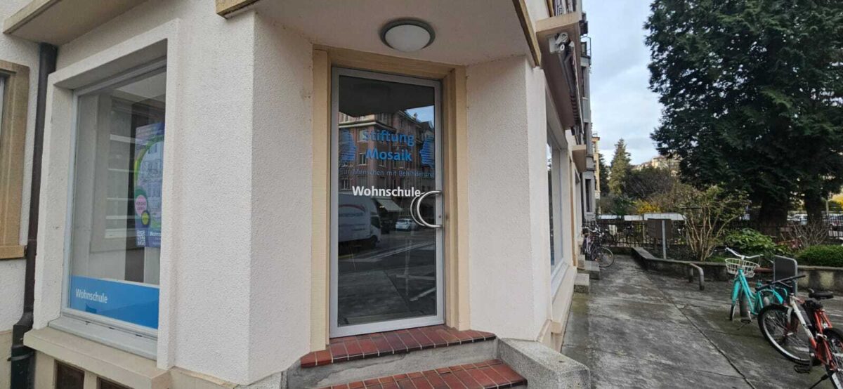"Eingang der Wohnschule der Stiftung Mosaik mit Glasfenstern und Fahrrädern davor."