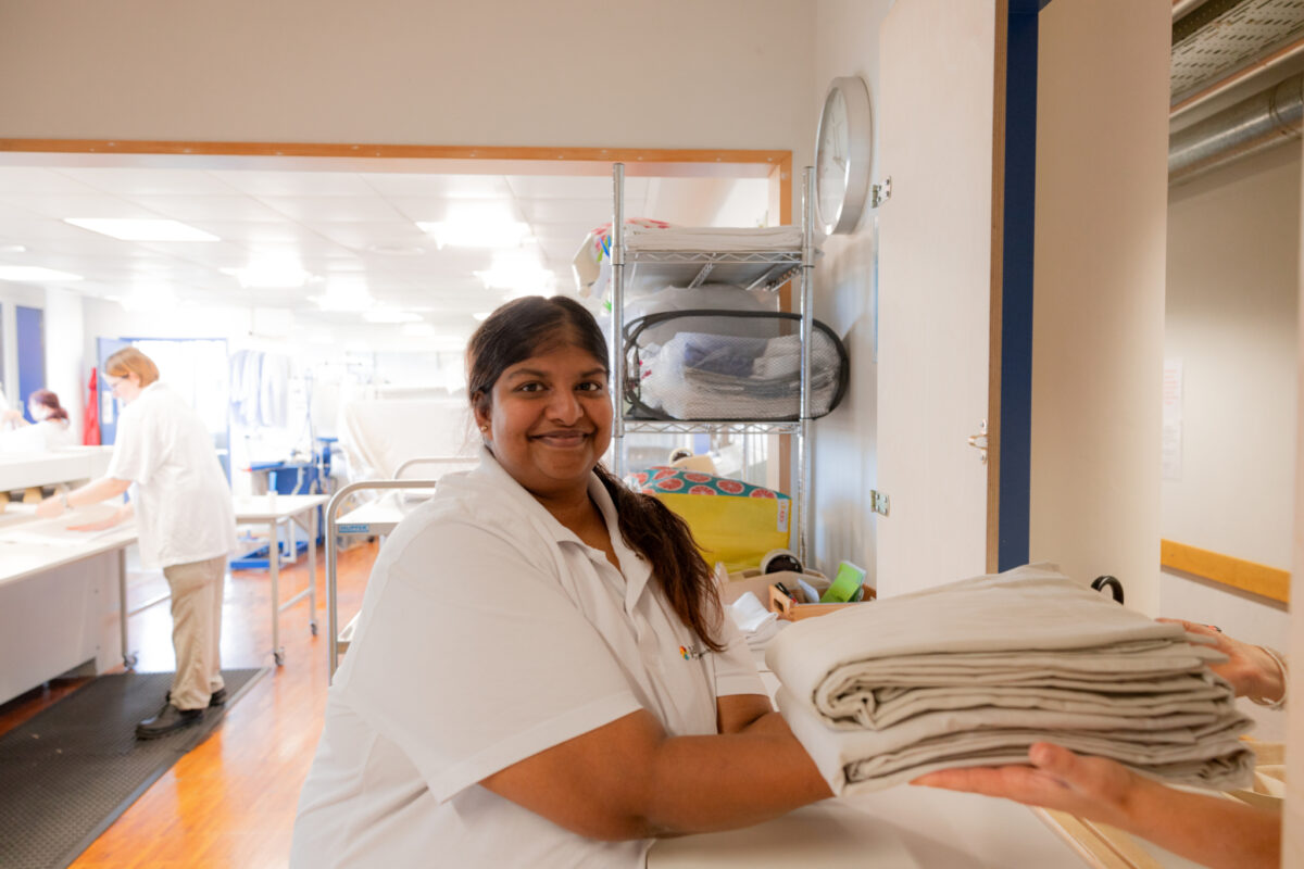 Eine Person in weißer Kleidung lächelt und hält gefaltete Tücher in einem Krankenhaus.