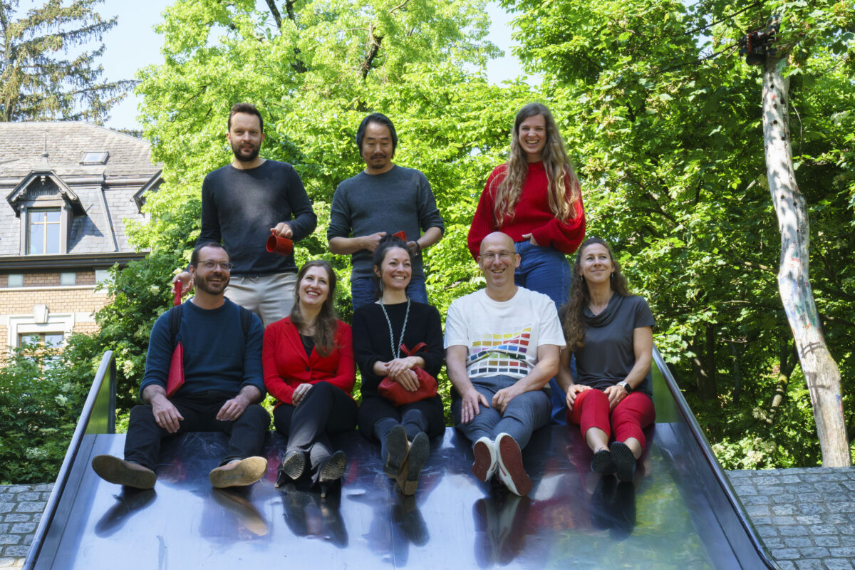 Eine Gruppe von sieben Personen sitzt auf einer Rutsche im Freien und lächelt.