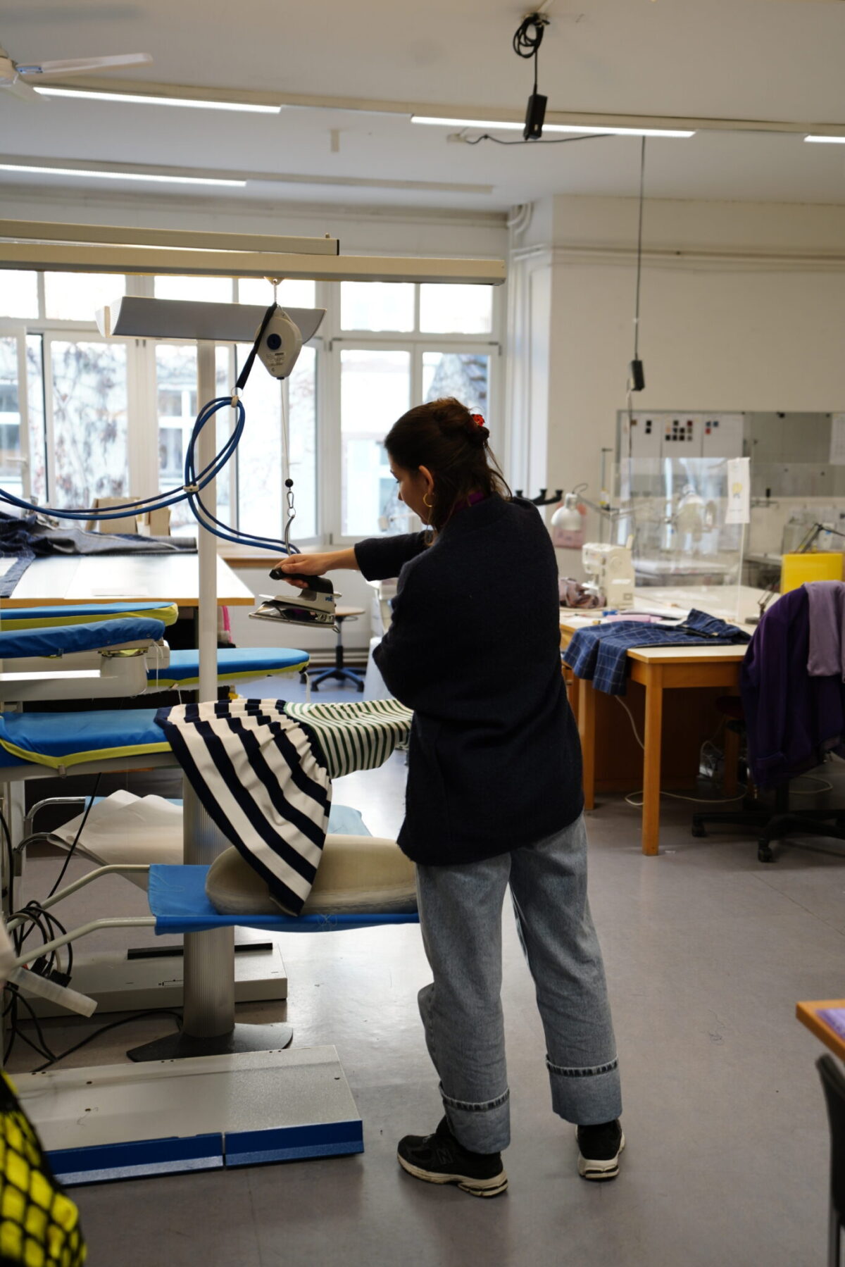 Eine Person bügelt ein gestreiftes Kleidungsstück in einem Nähraum.