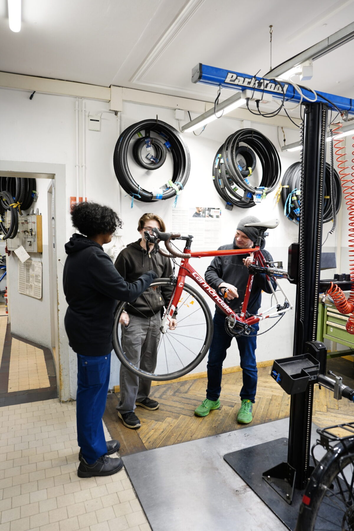 Drei Personen arbeiten in einer Fahrradwerkstatt an einem roten Fahrrad.