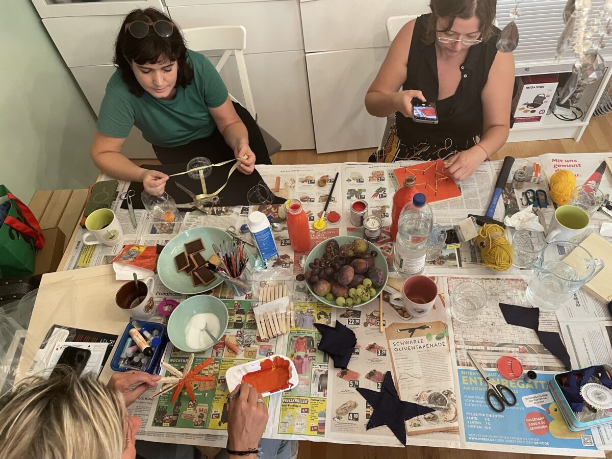 Drei Personen basteln gemeinsam an einem Tisch mit verschiedenen Materialien.