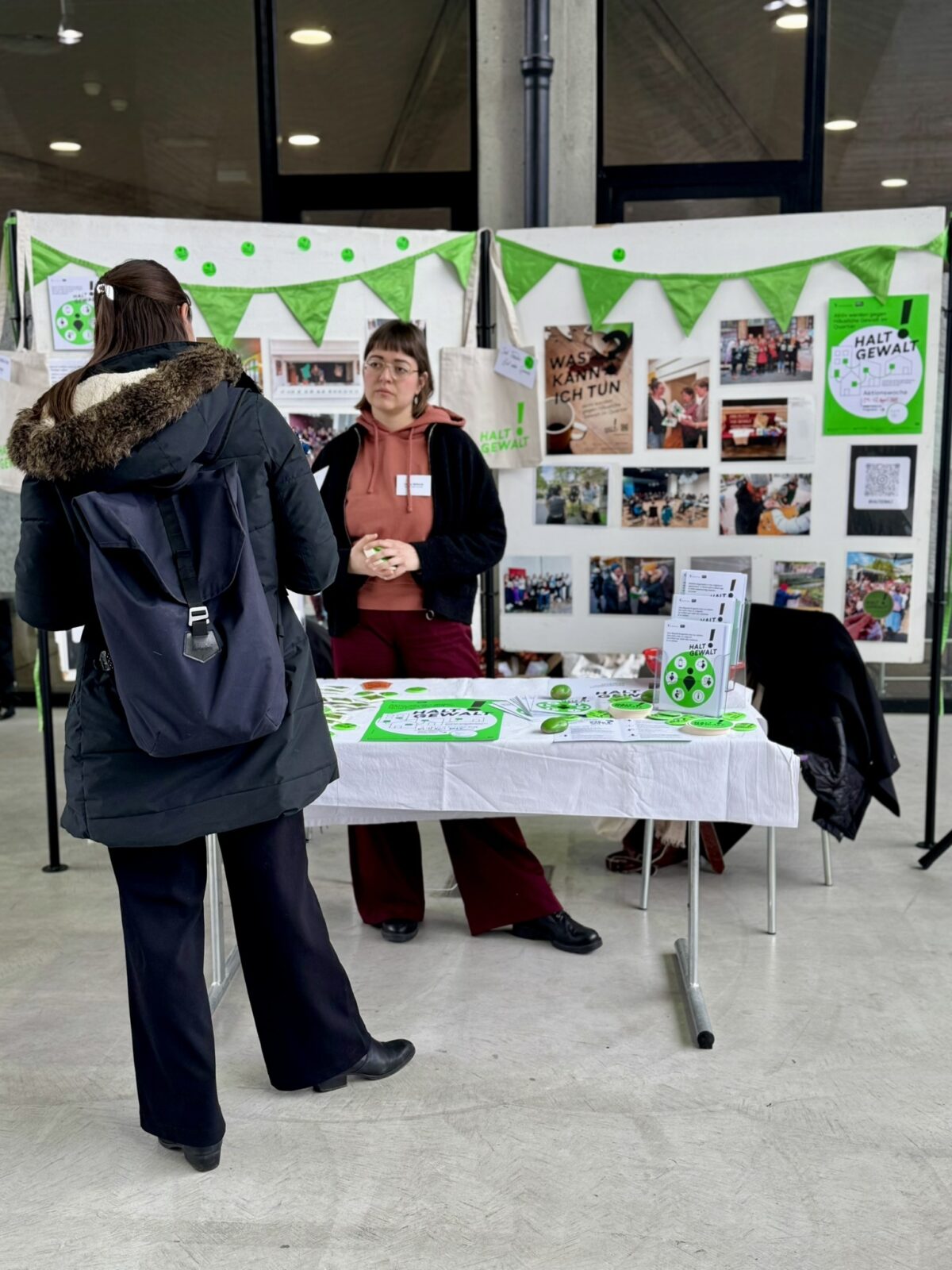 Zwei Personen stehen an einem Informationsstand mit Plakaten und Materialien zum Thema Gewaltprävention.