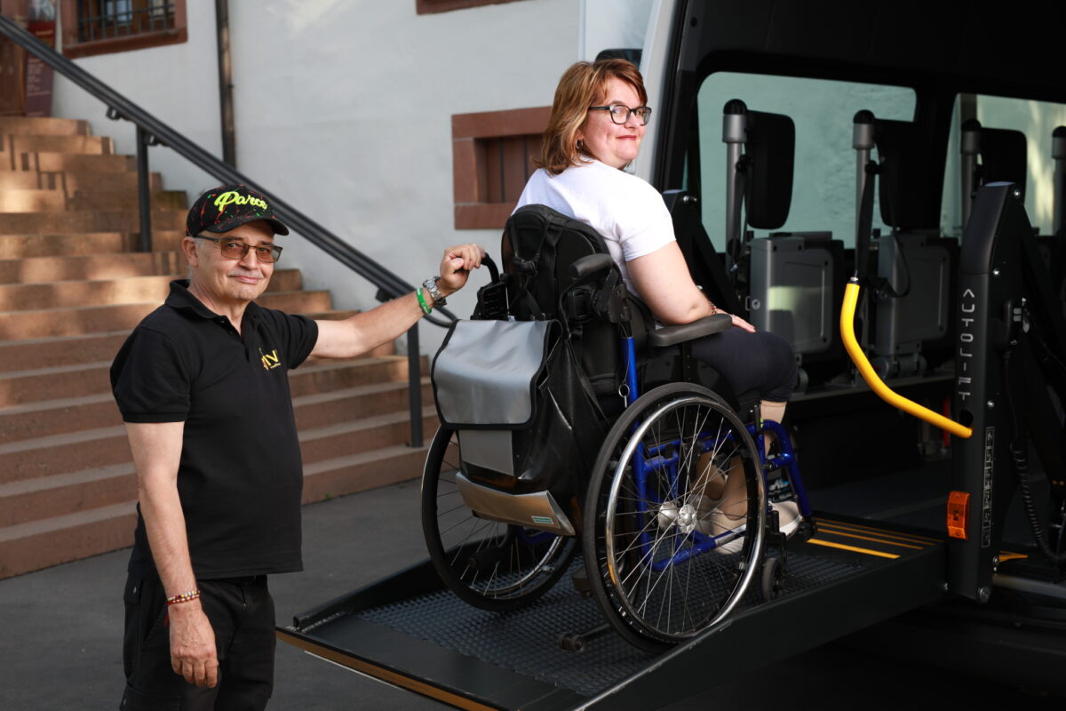 Eine Person im Rollstuhl wird von einer Rampe in einen Wagen gehoben.
