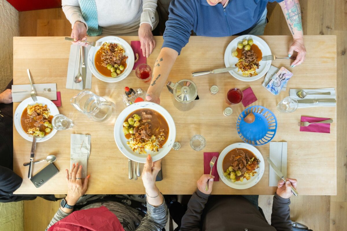 Eine Gruppe von Menschen sitzt an einem Tisch und isst gemeinsam ein Gericht.