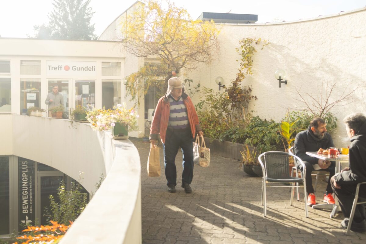 Eine Person geht an einem Café vorbei, während zwei andere an einem Tisch sitzen.