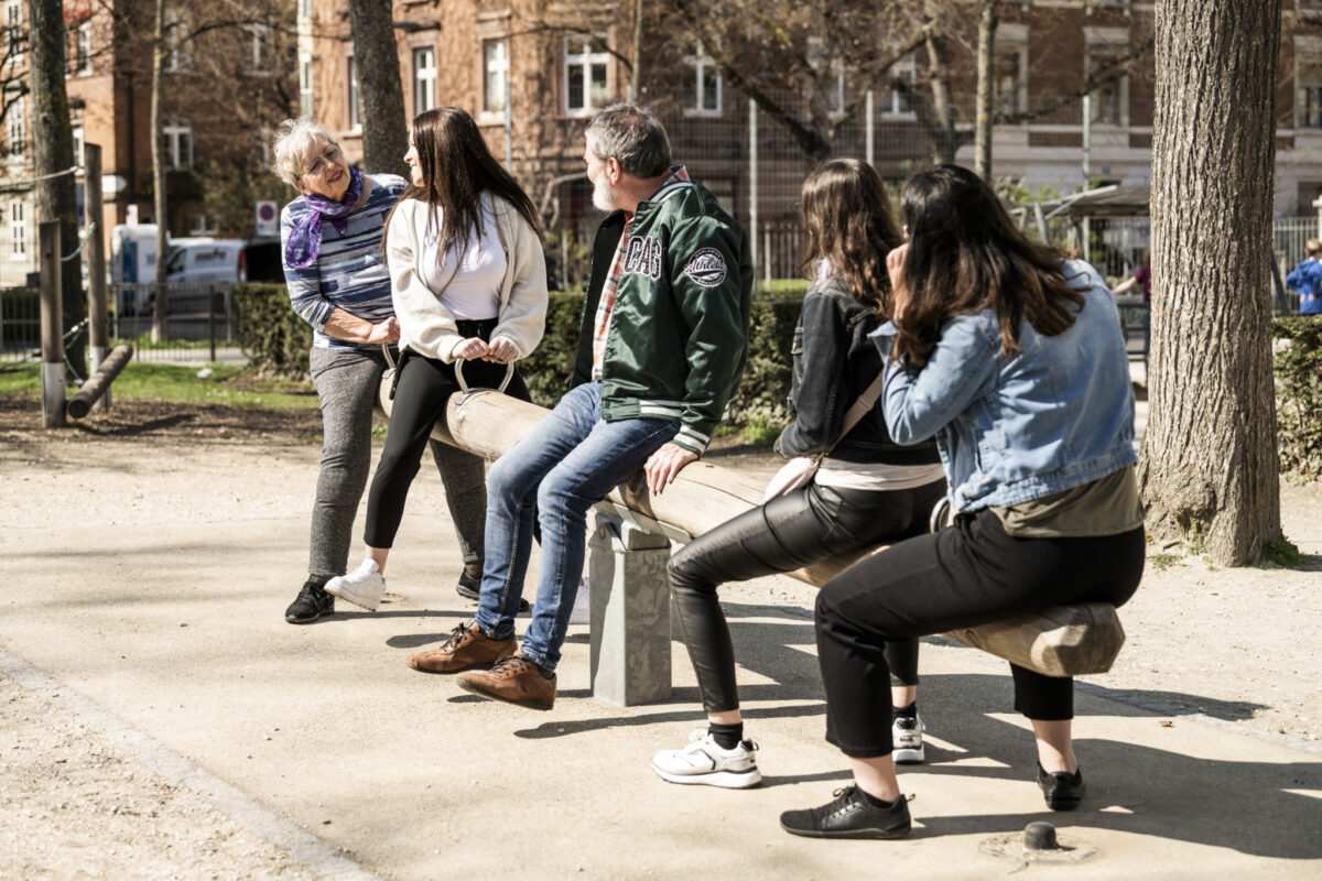 Eine Gruppe von Menschen unterhält sich im Park auf einer Bank.