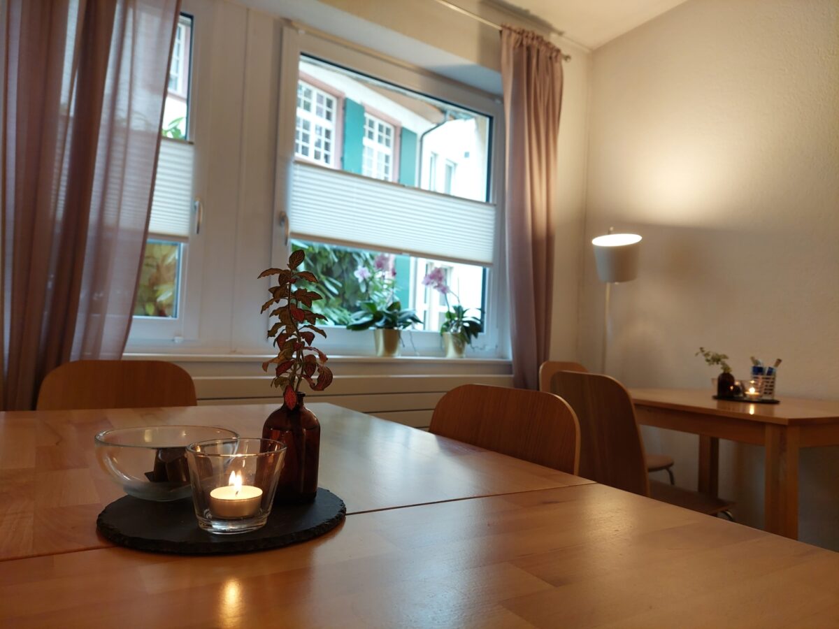 Ein Tisch mit Kerzen und einer Pflanze vor einem hellen Fenster.