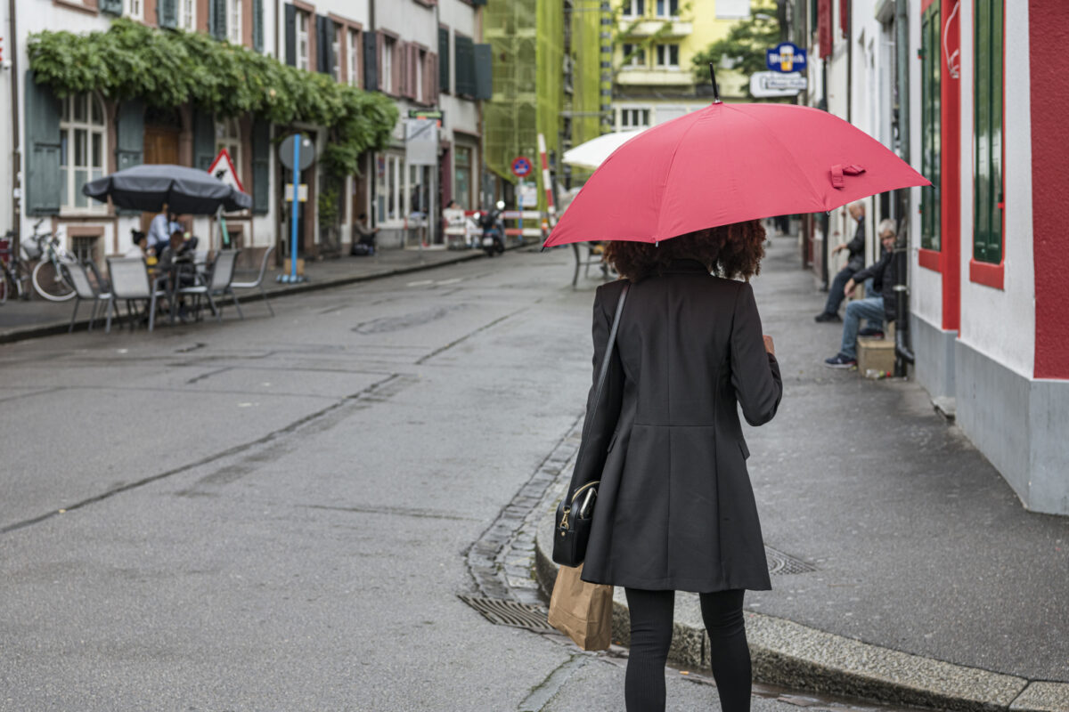 Eine Person mit rotem Regenschirm geht eine Straße entlang.