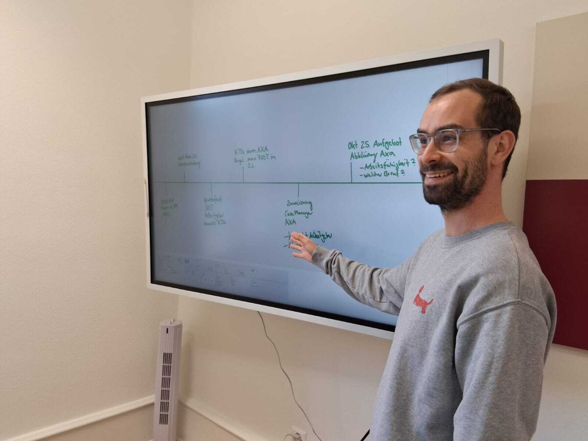 Ein Mann schreibt an ein digitales Whiteboard und lächelt.