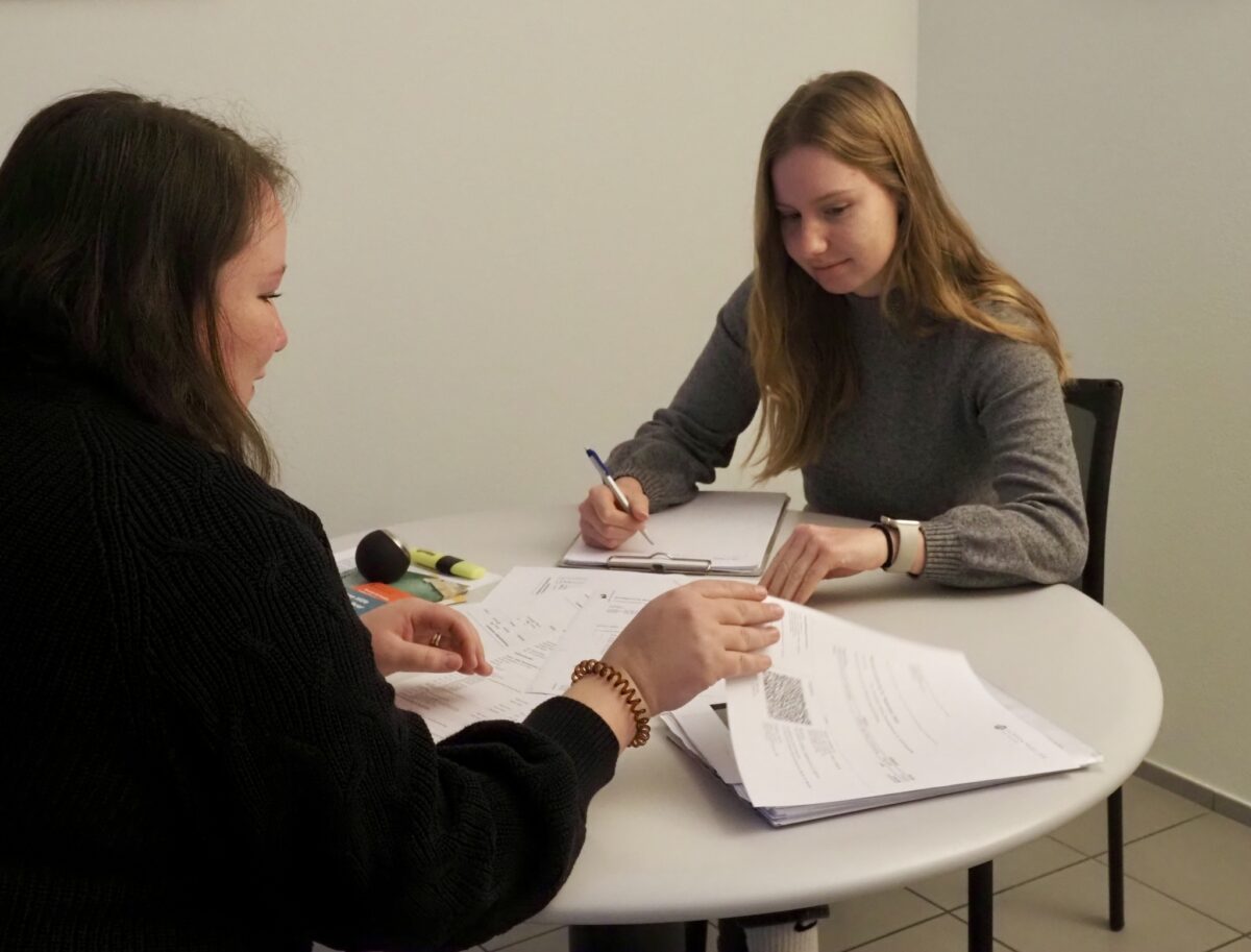 Zwei Personen führen ein Gespräch an einem Tisch mit Unterlagen.