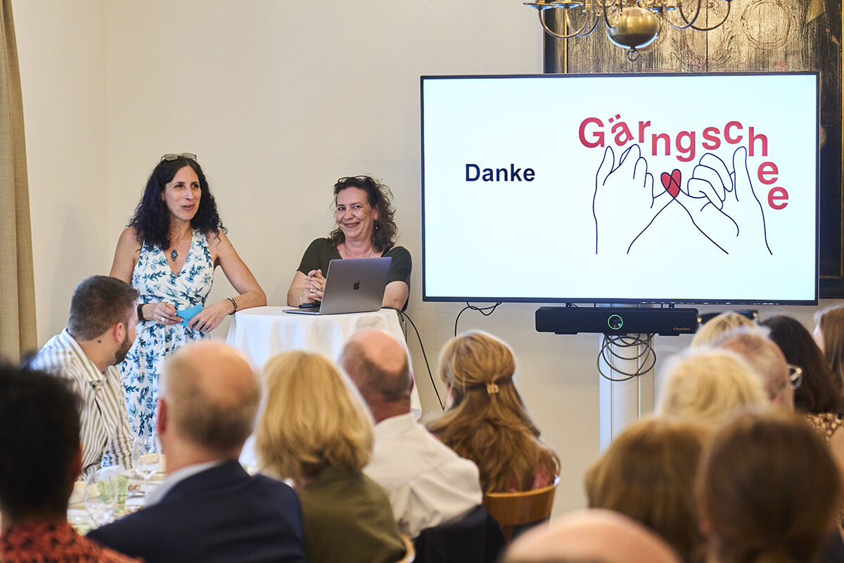 Zwei Frauen halten eine Präsentation mit dem Titel "Danke Gärngschee" vor Publikum.