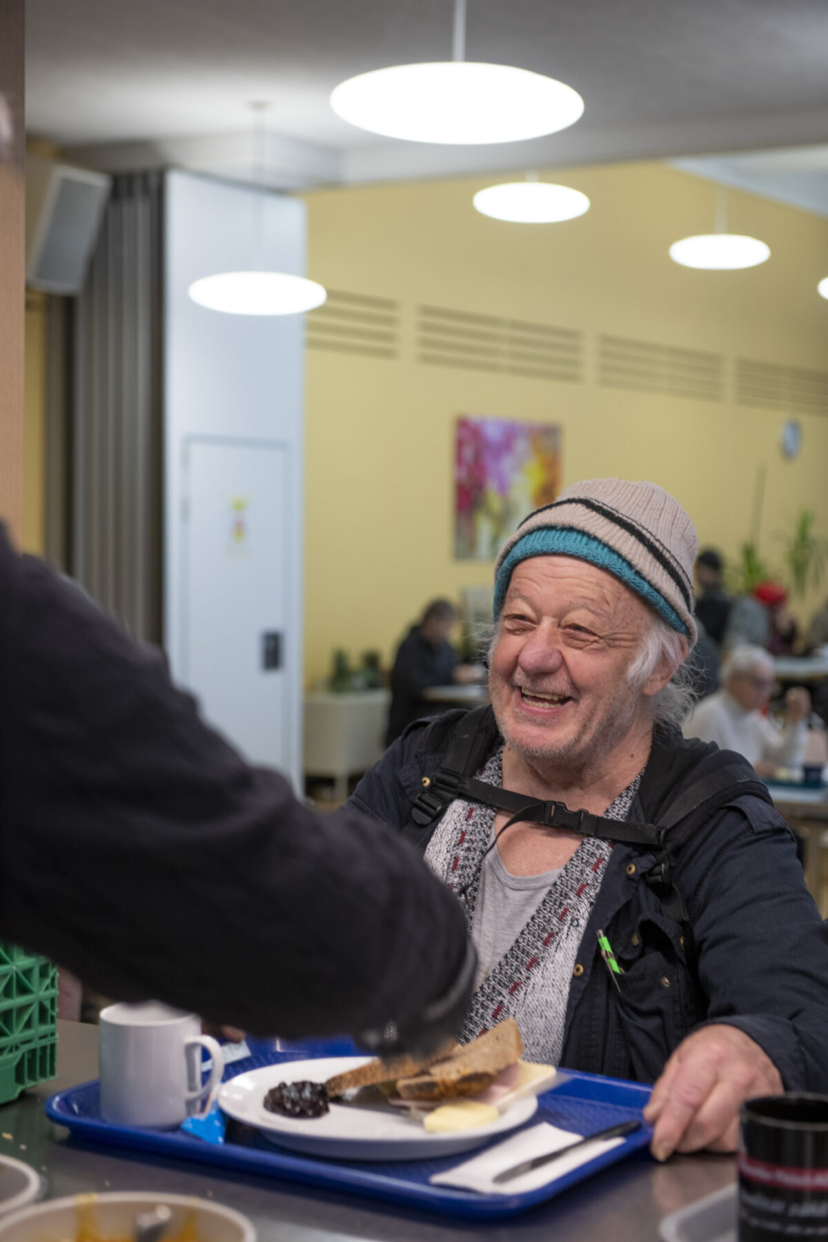Ein älterer Mann lacht fröhlich in einer Cafeteria.