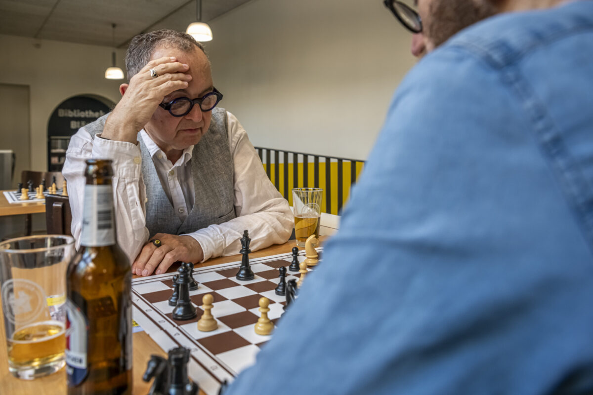 Zwei Männer spielen Schach in einem Café und trinken Bier.