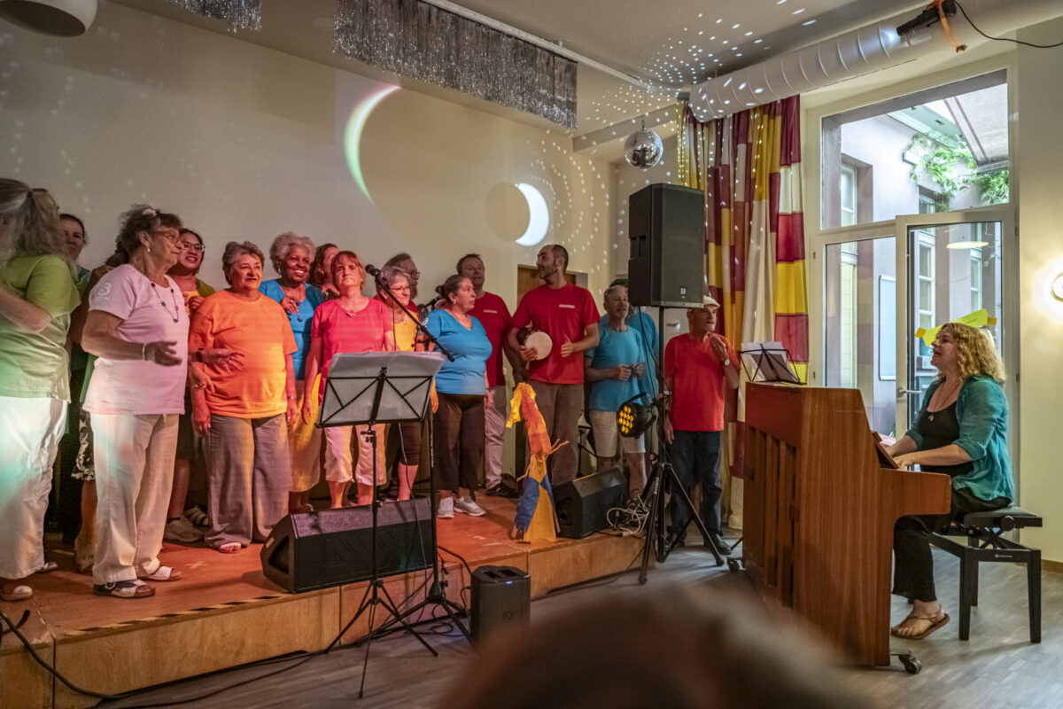 Eine Gruppe von Menschen singt auf einer Bühne mit einem Pianisten.