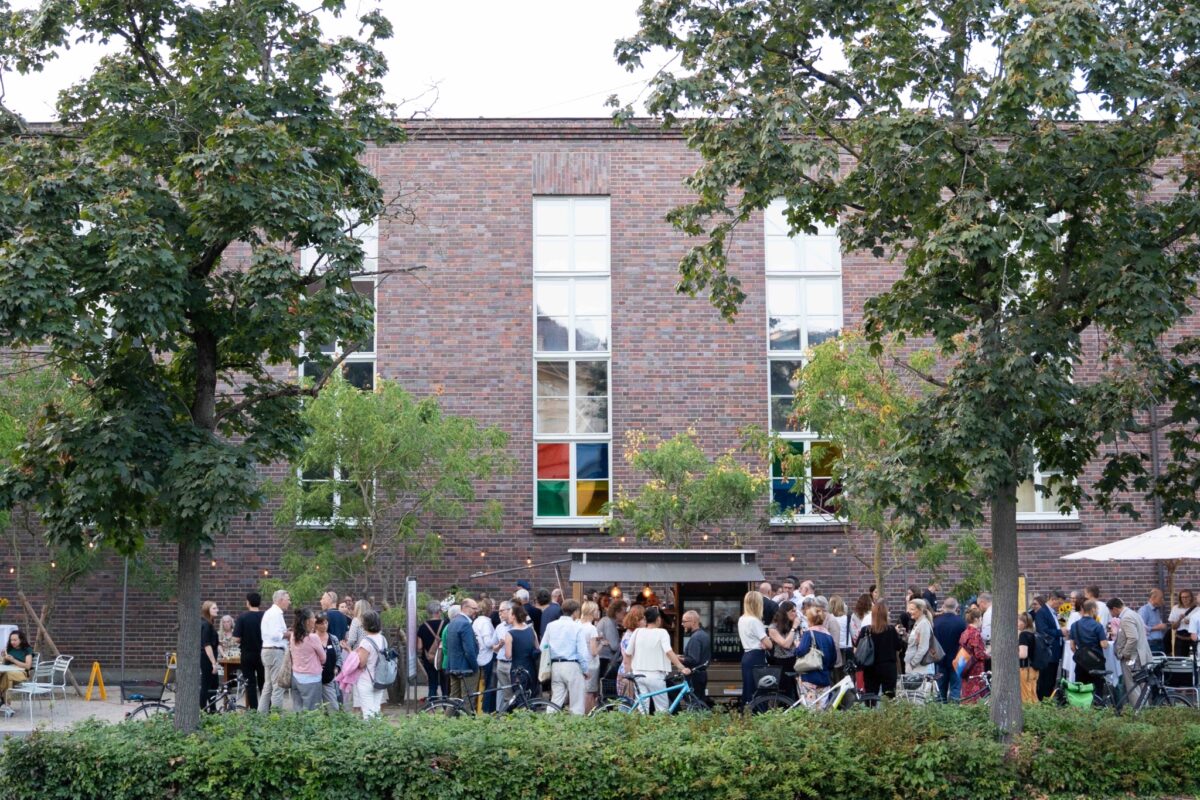 Eine Gruppe von Menschen steht vor einem Backsteingebäude und unterhält sich.