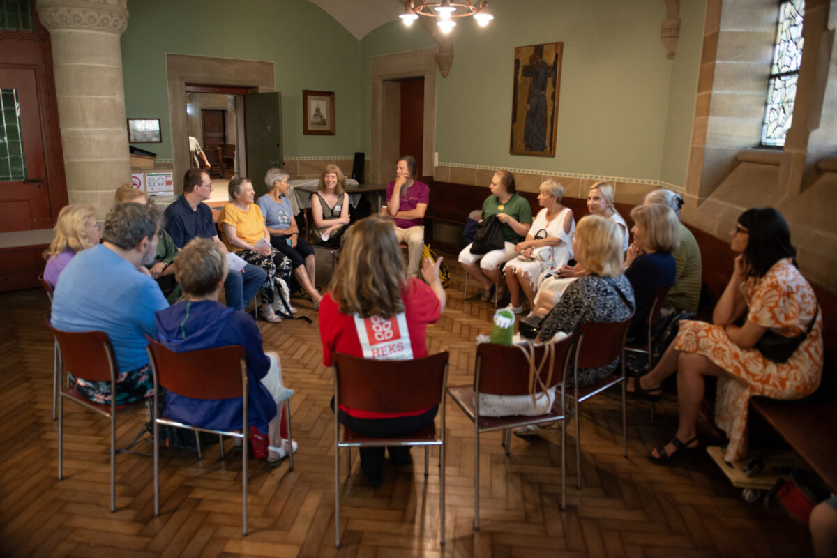 Eine Gruppe von Menschen sitzt im Kreis und unterhält sich in einem Raum.