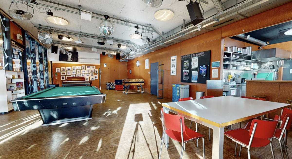 Ein gemütlicher Raum mit Billardtisch, Tischen und Stühlen, dekoriert mit Bildern und Schildern.