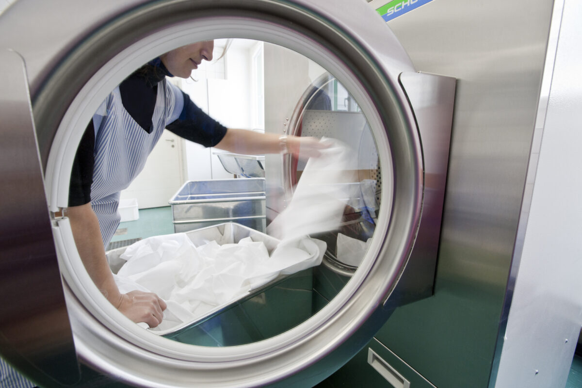 Eine Person entnimmt Wäsche aus einem großen Wäschetrockner.