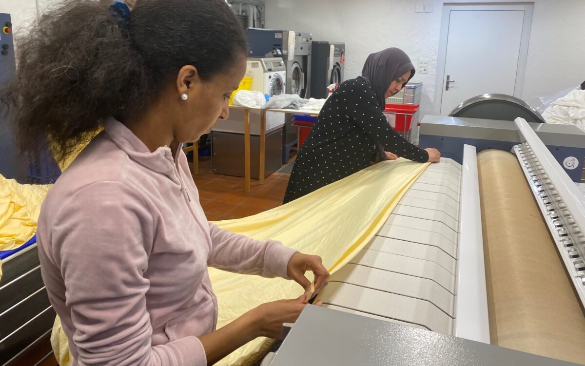 Zwei Frauen arbeiten an einer Textilmaschine mit gelbem Stoff.