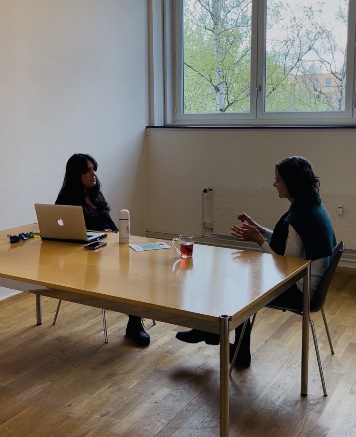 Zwei Personen führen ein Gespräch an einem Tisch mit Laptop und Getränken.