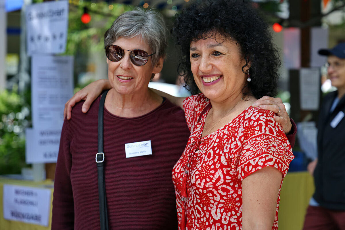 Zwei Frauen lächeln und umarmen sich bei einer Veranstaltung.