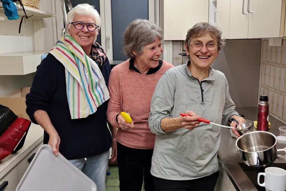 Drei Frauen lächeln in einer Küche und bereiten gemeinsam etwas zu.