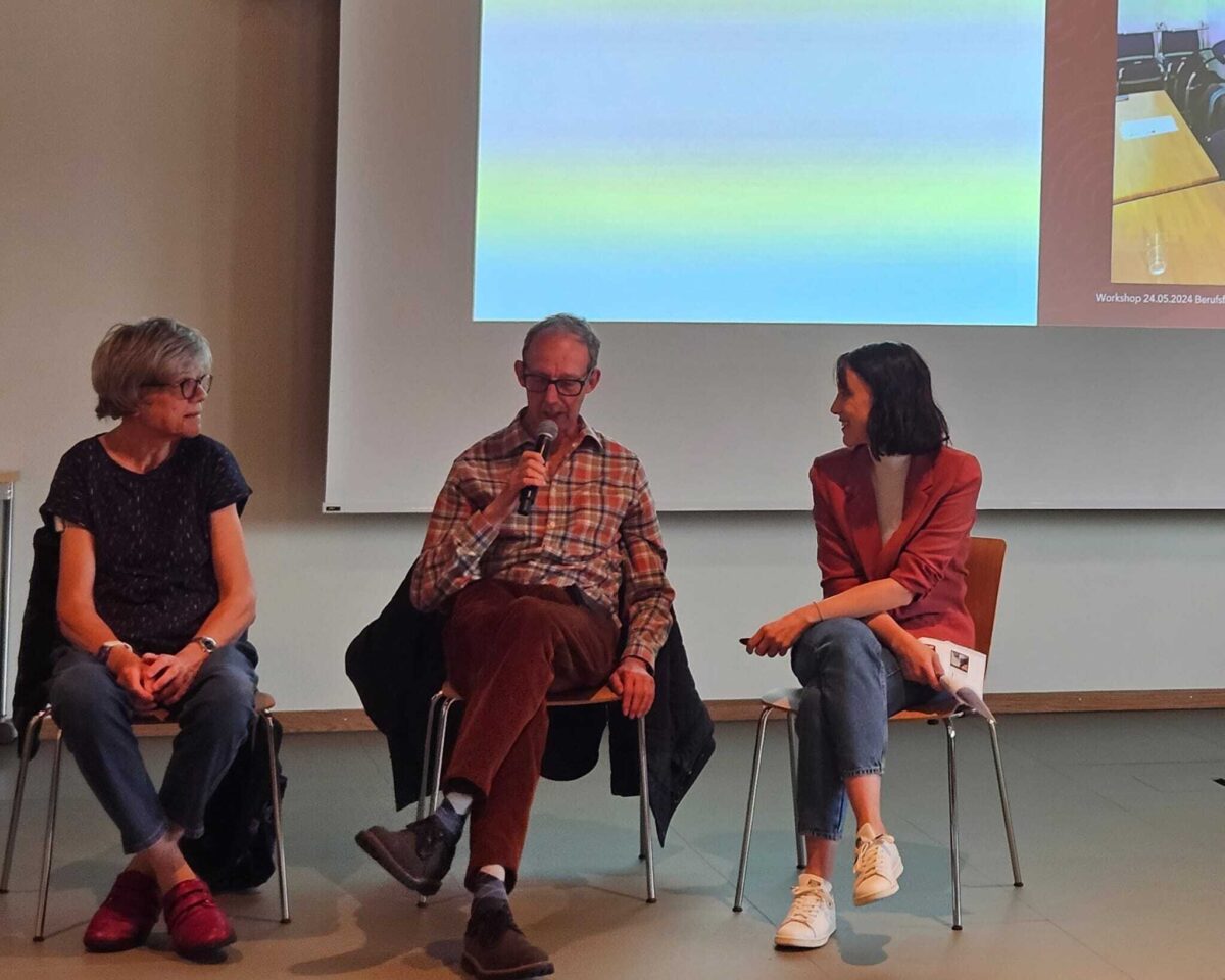 Drei Personen sitzen auf einer Bühne und diskutieren während eines Workshops.