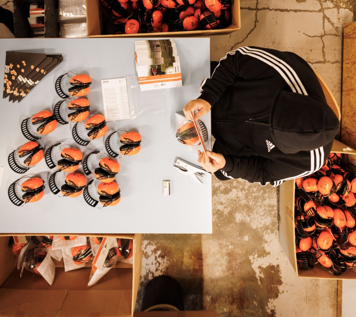 Eine Person sortiert orangefarbene Gehörschutzausrüstung auf einem Tisch.