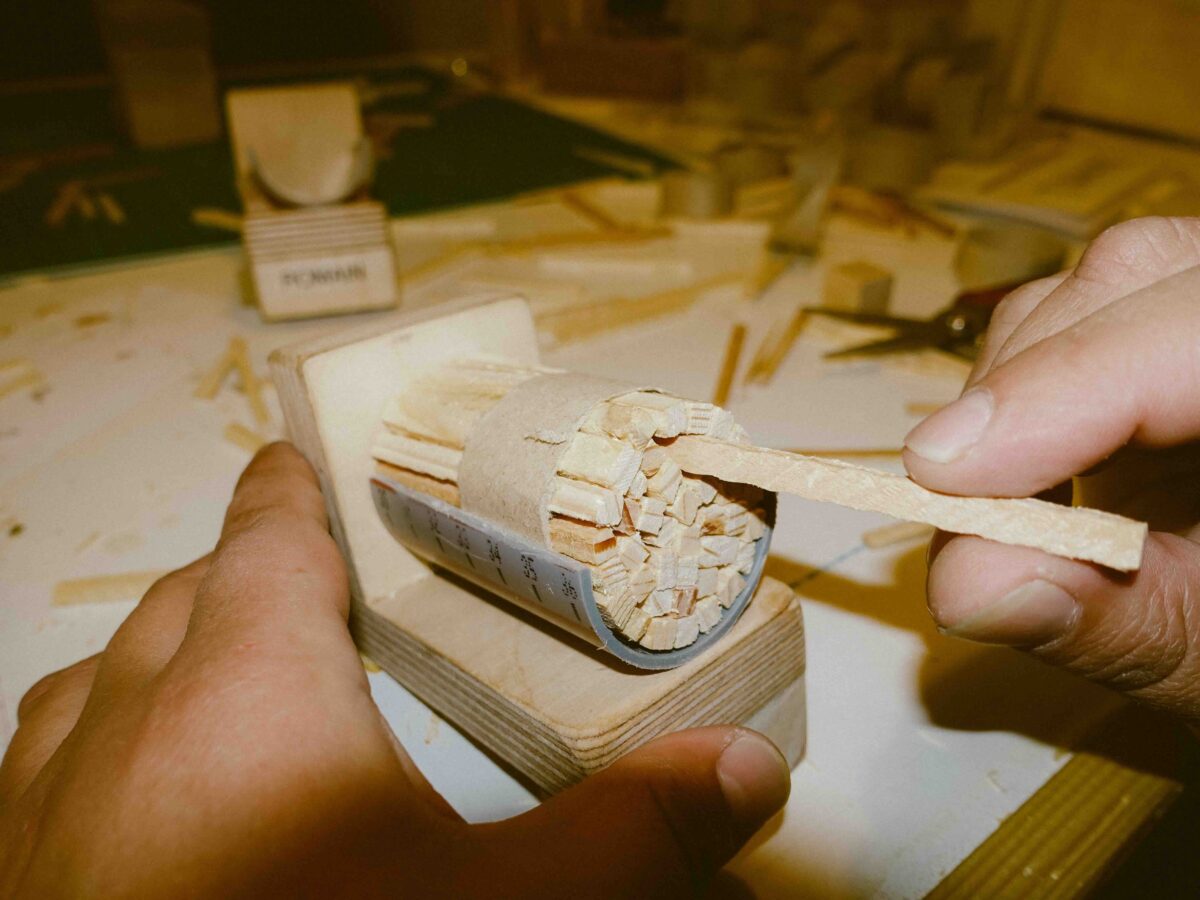 Hände schaben Holzspäne von einem Holzblock mit einem Schaber.