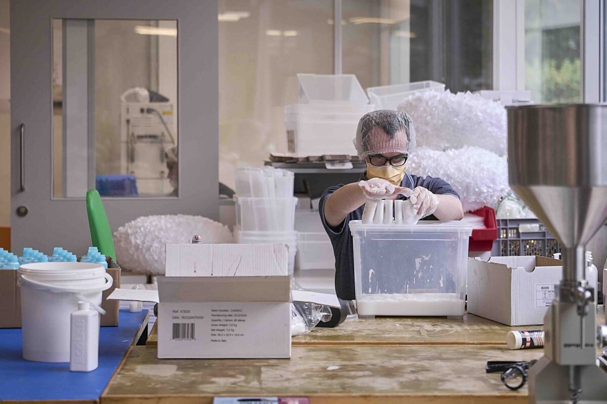 Eine Person in Schutzausrüstung füllt in einer Werkstatt Behälter mit Material.