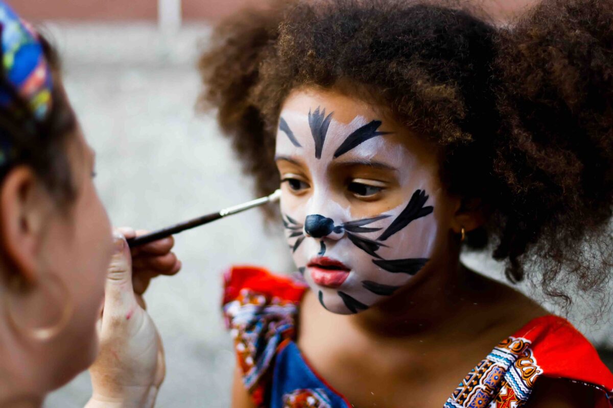 Ein Kind bekommt ein Katzengesicht als Gesichtsschminkung aufgemalt.