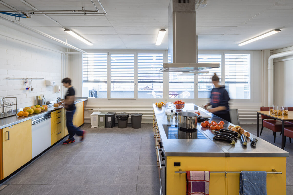 Zwei Personen arbeiten in einer modernen Küche mit großen Fenstern.