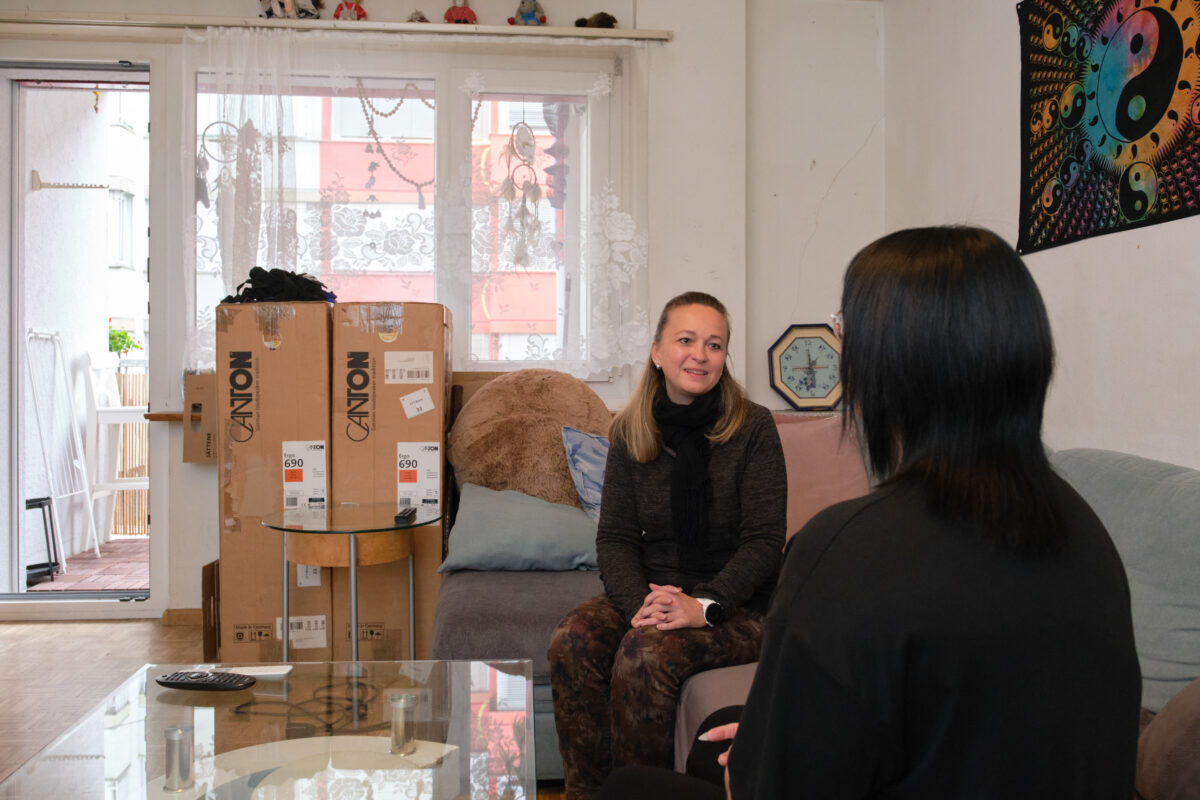 Zwei Personen sitzen auf einem Sofa und unterhalten sich in einem Wohnzimmer.