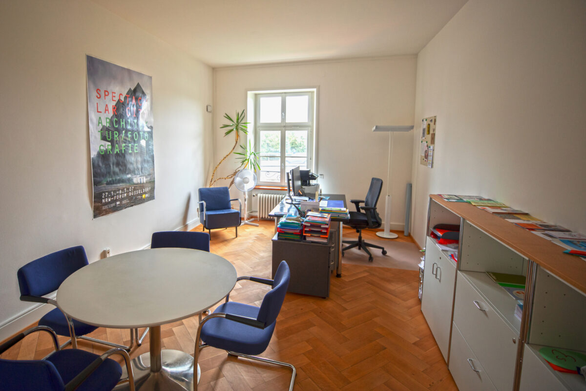 Ein helles Büro mit Schreibtisch, Stühlen und einem runden Tisch.