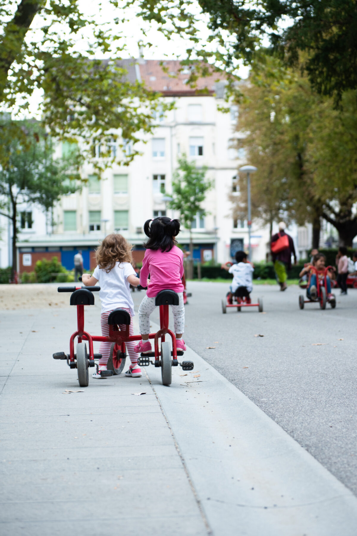 Zwei Kinder fahren auf kleinen Fahrrädern eine Straße entlang.
