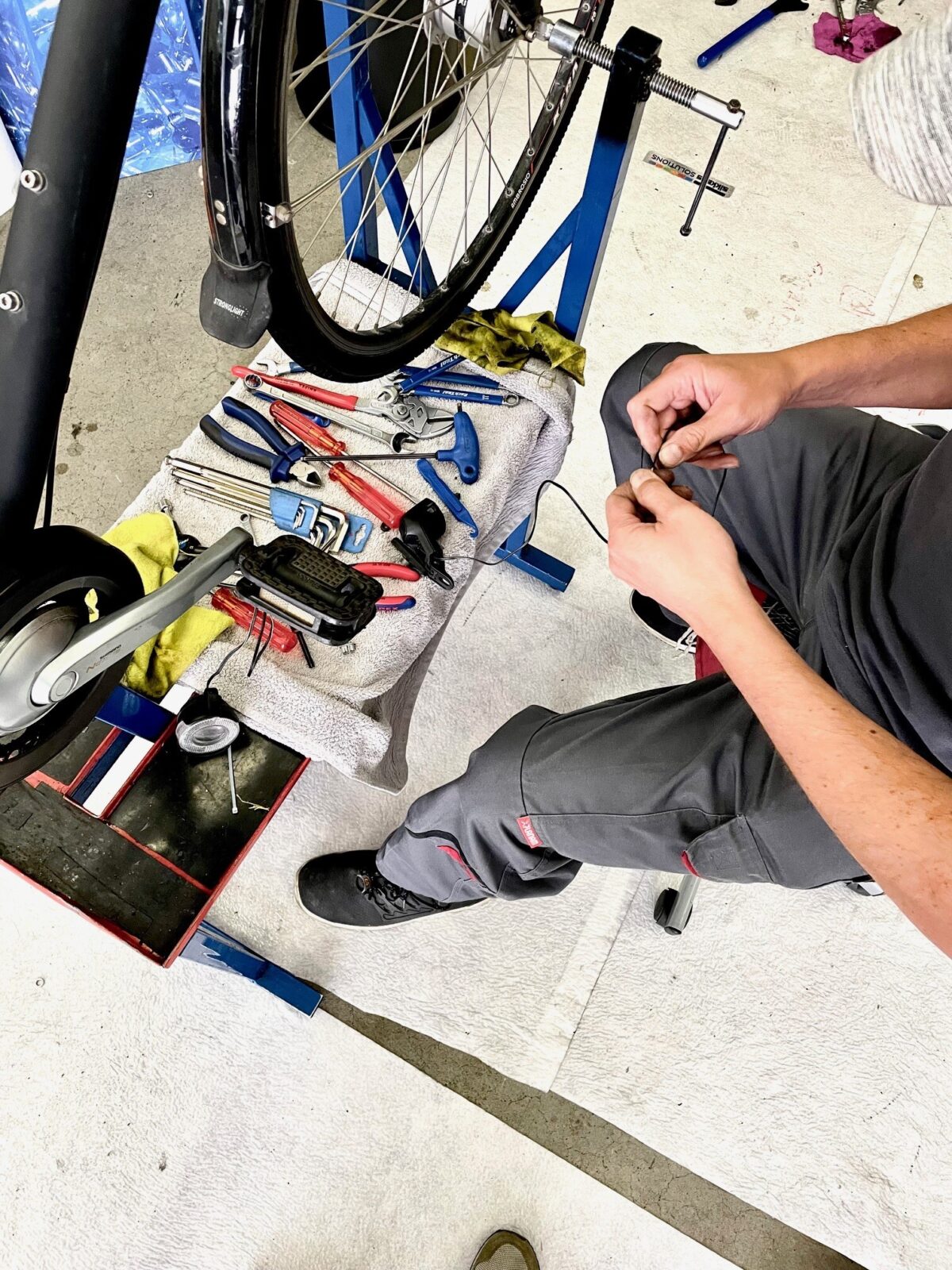 Eine Person repariert ein Fahrrad und hält ein Werkzeug in der Hand.