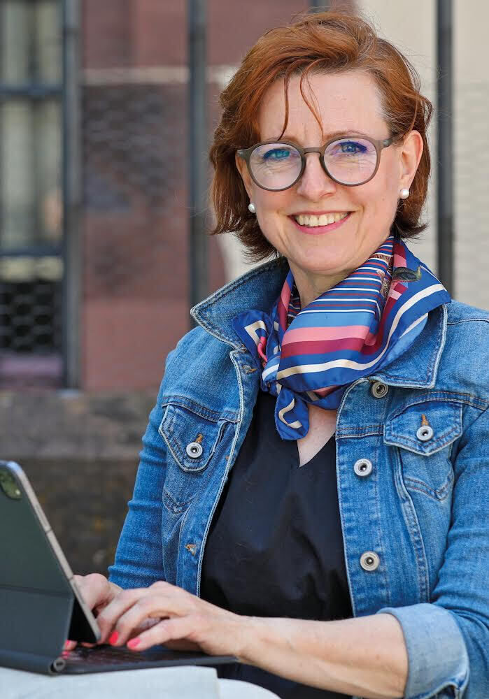 Eine lächelnde Frau mit Brille arbeitet an einem Laptop.