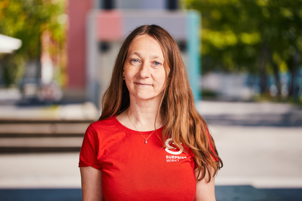 Eine Frau mit langem Haar lächelt in einem roten T-Shirt mit Aufdruck.